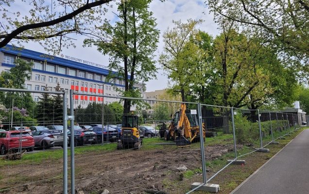 widok przedniego wjazdu do Wojskowgo Instytutu Medycznego od ulicy Szaserów. Na zdjęciu znajduje sie rozkopana cześć ogrodzenia z koparkami pokazujące rozpoczęty remont