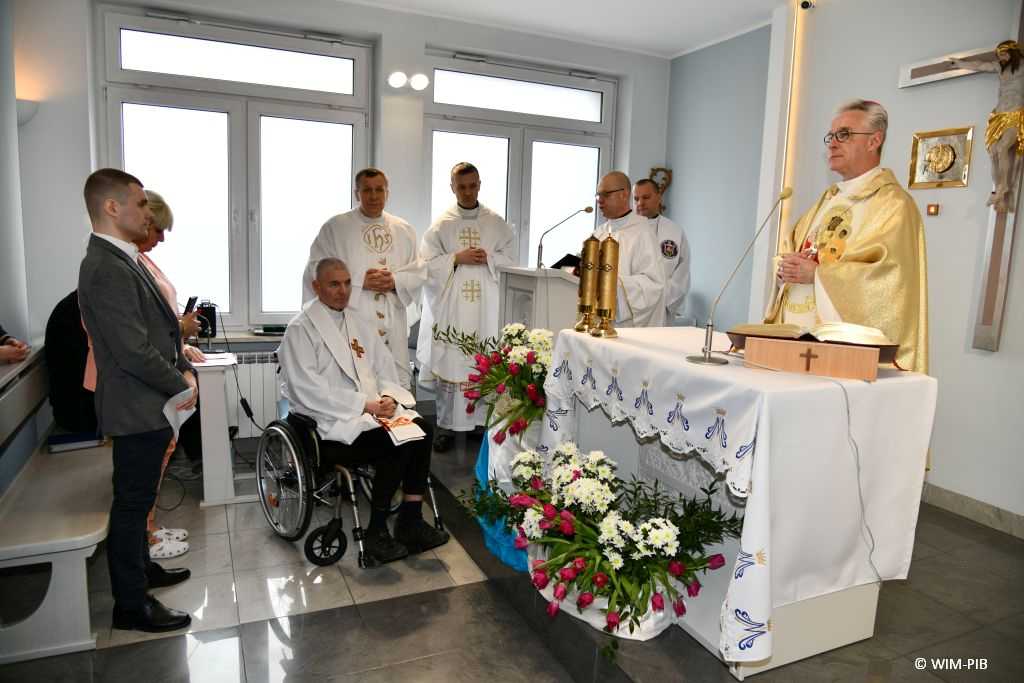 Msza święta z okazji dnia chorego w kaplicy szpitalnej Wojskowego Instytutu Medycznego. Zdjęcie biskupa polowego podczas odprawianej mszy. Obok ksiadz na wózku uczestniczy w mszy, obok niego modlący się księża.