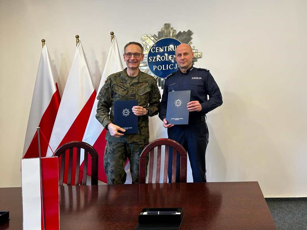 generał broni prof. dr hab. Grzegorz Gielerak i insp. Ryszard Jakubowski Komendant Centrum Szkolenia Policji w Legionowie pozują do zdjęcia po podpisaniu umowy. W rękach prezentują teczki z podpisaną umową.