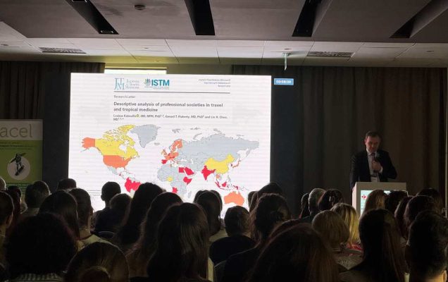 Słuchacze siedzący na sali podczas wykładu na konferencji. Widok z końca sali. Ma slajdzie Mapa świata.