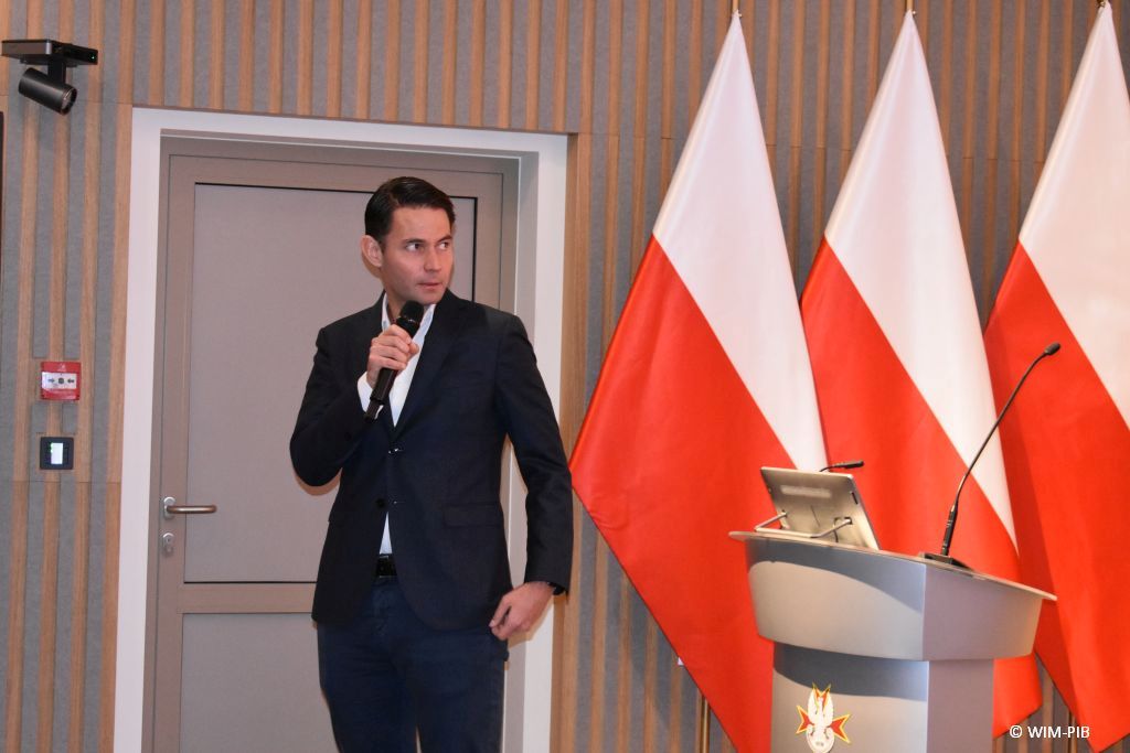 Prelegent konferencji z mikrofonem w dłoni.