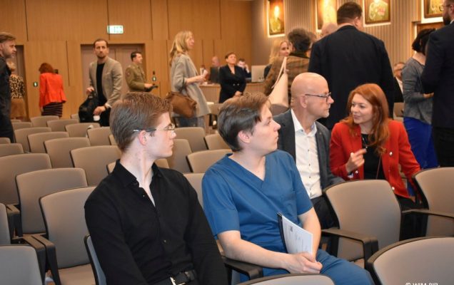 Fragment auli podczas przerwy. Na pierwszym planie 2 siedzących lekarzy, jeden z nich ubrany w strój chirurgiczny.