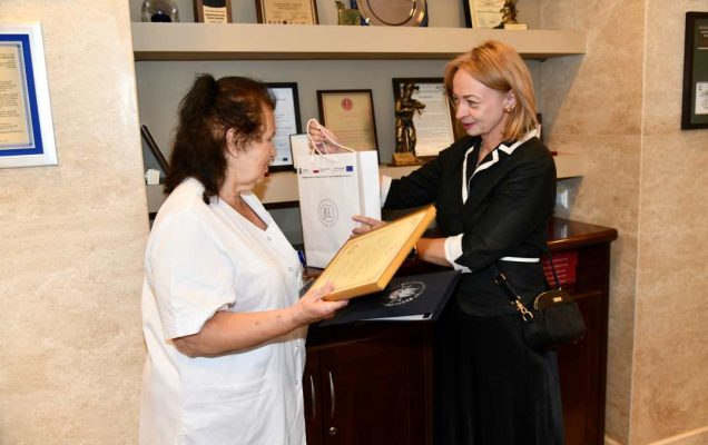 Alicja Rączka z dyplomem w rękach obok niej Monika Pintal -Ślimak wręcza upominek Pani Alicji.