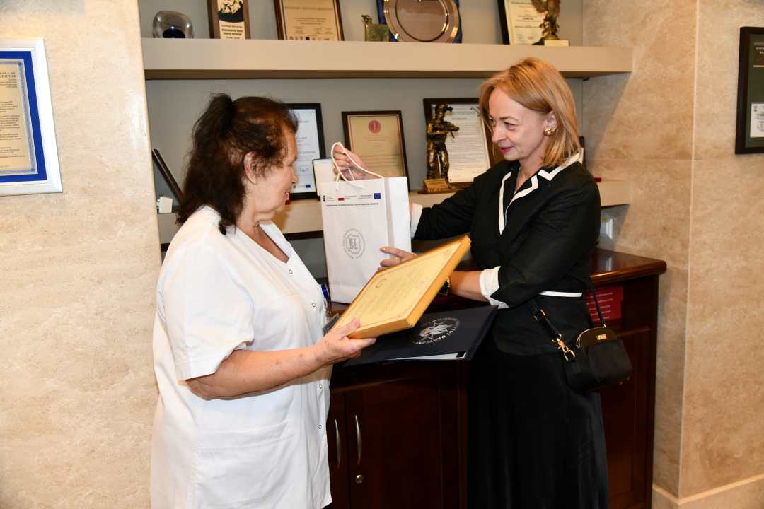 Alicja Rączka z dyplomem w rękach obok niej Monika Pintal -Ślimak wręcza upominek Pani Alicji.