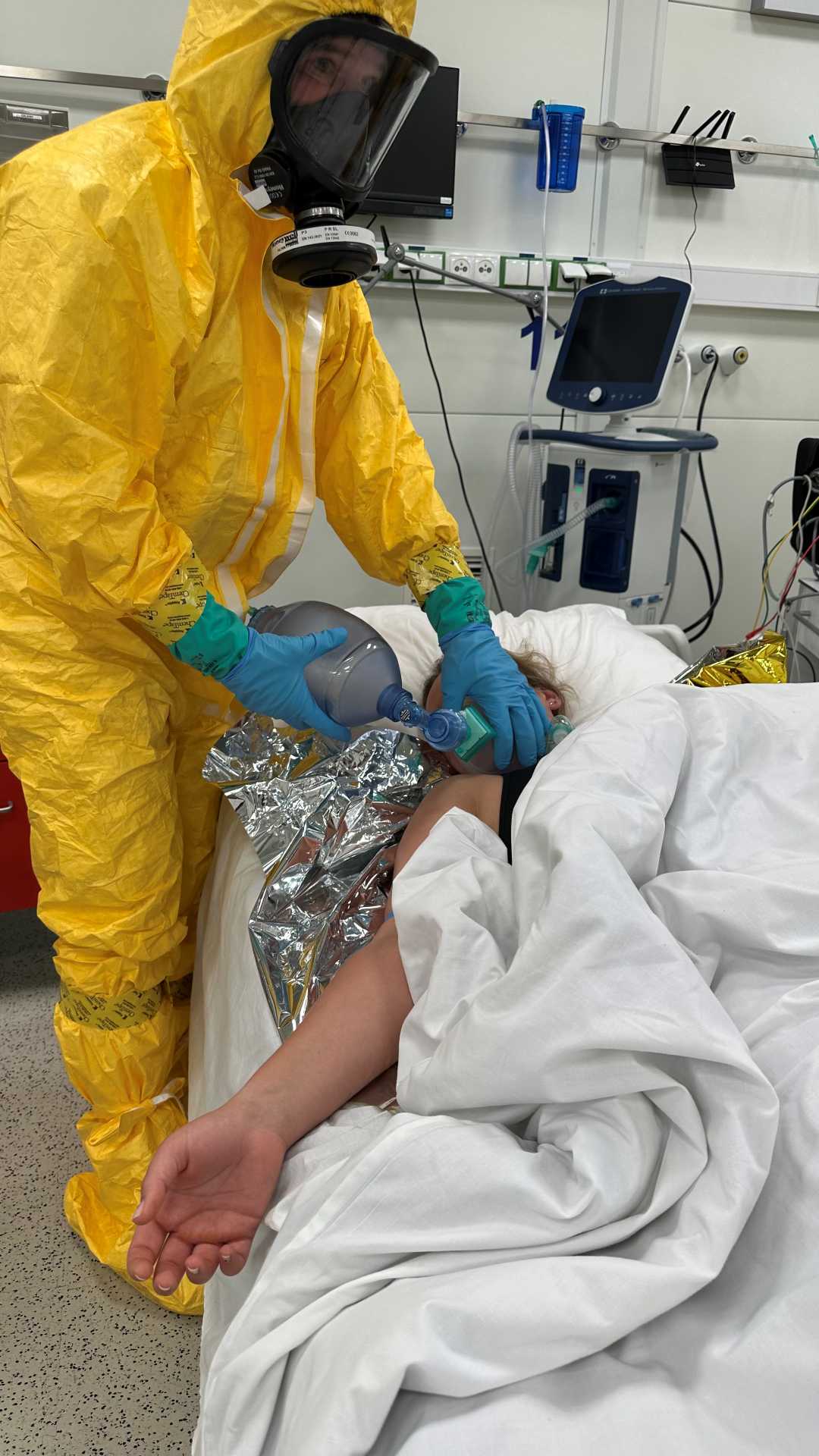 Medyk w żółtym kombinezonie i masce gazowej opatruje podczas ćwiczeń rannego.