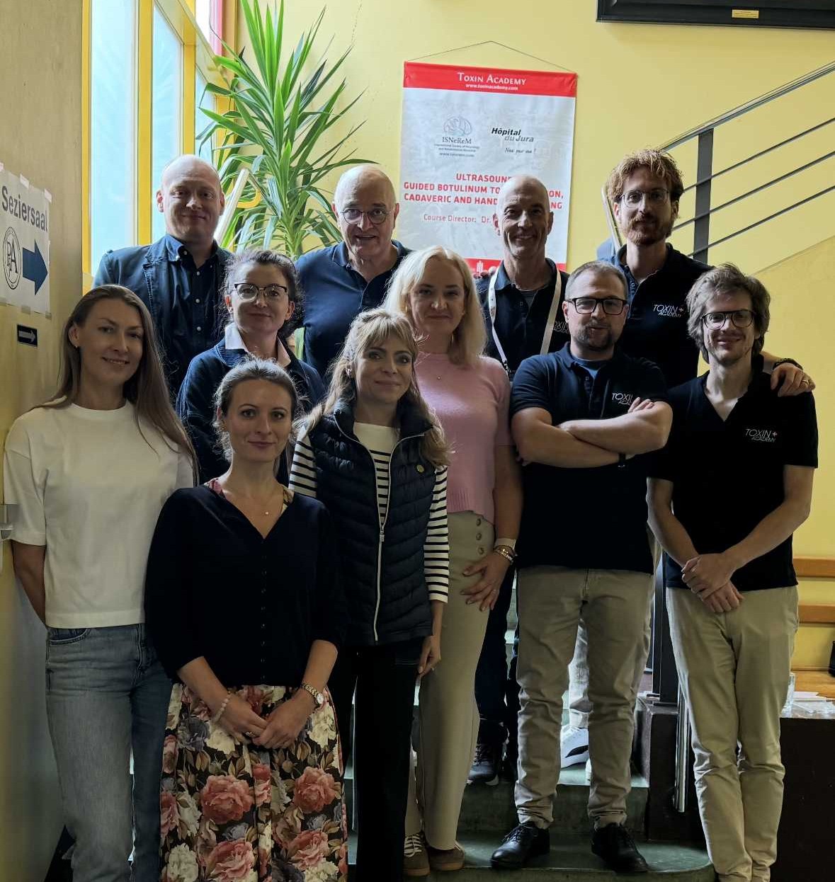 Zdjęcie grupowe na schodach wewnątrz budynku uczestników szkolenia Spasticity Management Masterclass.