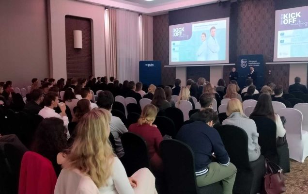 Ujęcie z tyłu sali. Uczestnicy konferencji na sali Konferencyjnej, na przeciw dwa ekrany wyświetlające materia konferencyjny.