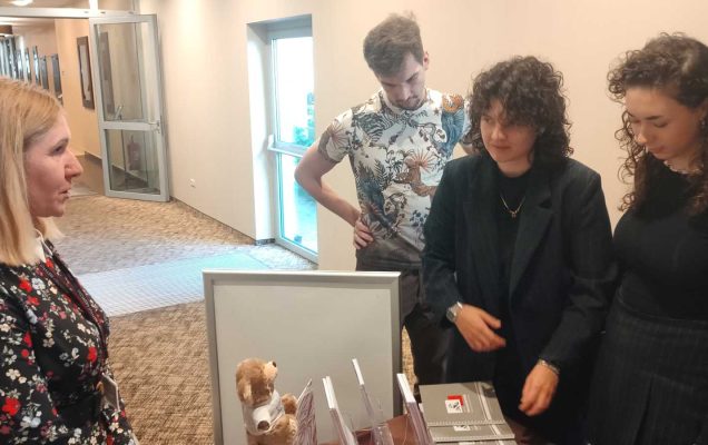 Pracownica WIM przy stoisku informacyjnym, obok niej studentki i studenci przeglądający materiały informacyjne.