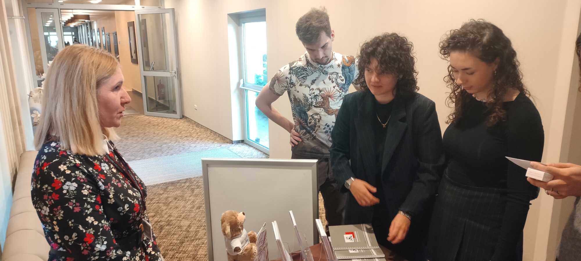 Pracownica WIM przy stoisku informacyjnym, obok niej studentki i studenci przeglądający materiały informacyjne.