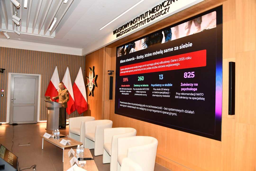 Prelegent przy mównicy za nim na wyświetlaczu fragment prezentacji.