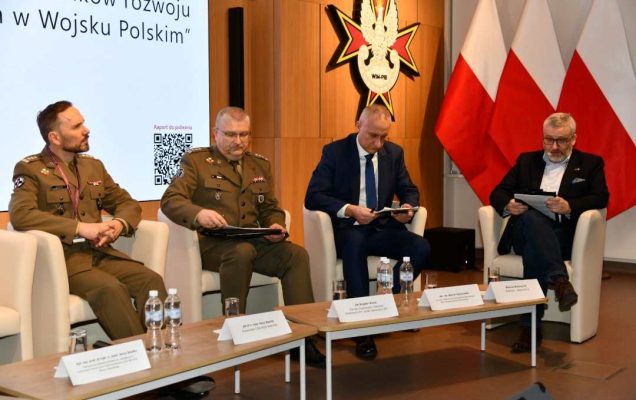 Uczestnicy siedzący w fotelach podczas panelu dyskusyjnego, za ich plecami wyświetlony fragment prezentacji.