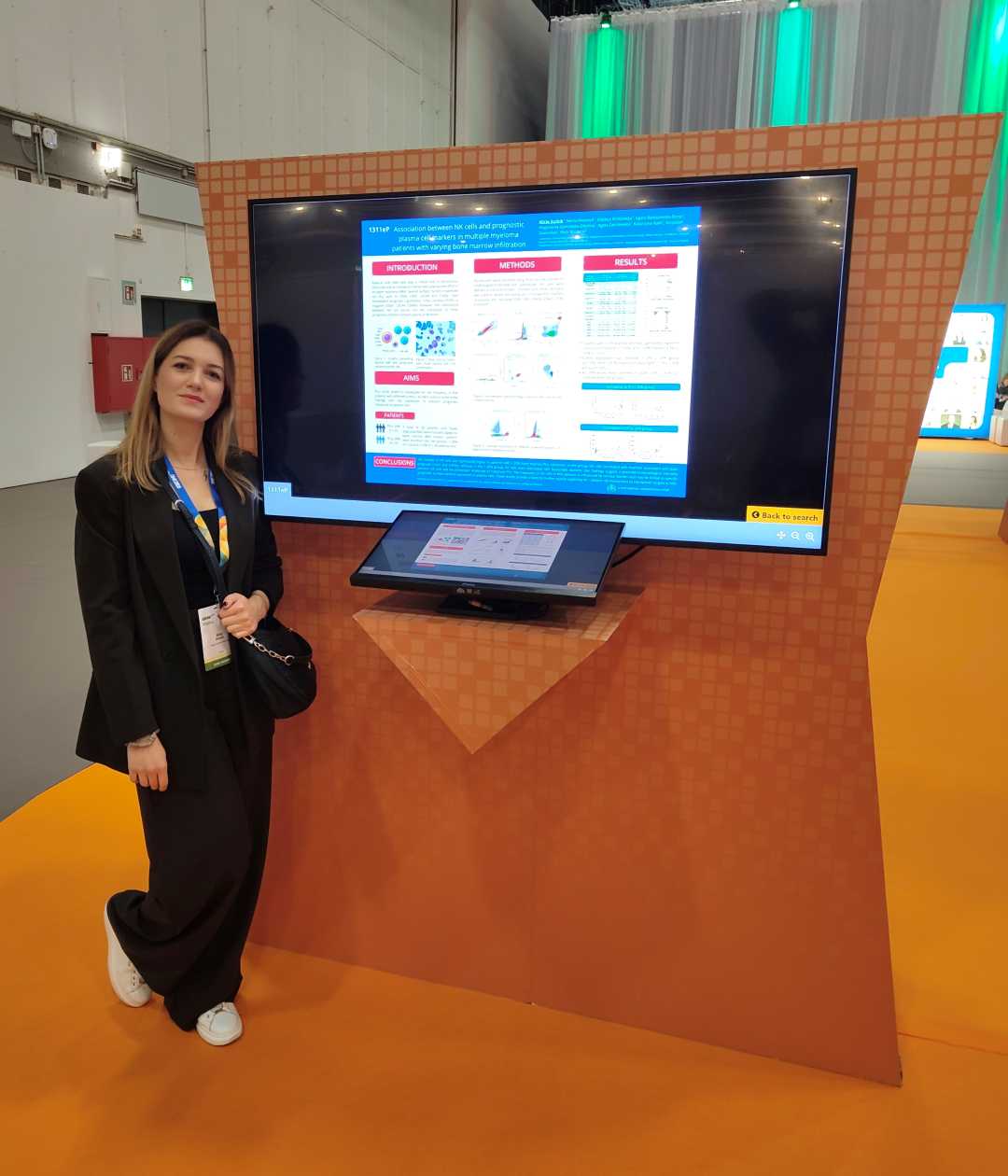 Alicja Dudzik stoi przy wyświetlaczu z plakatem w holu konferencyjnym.