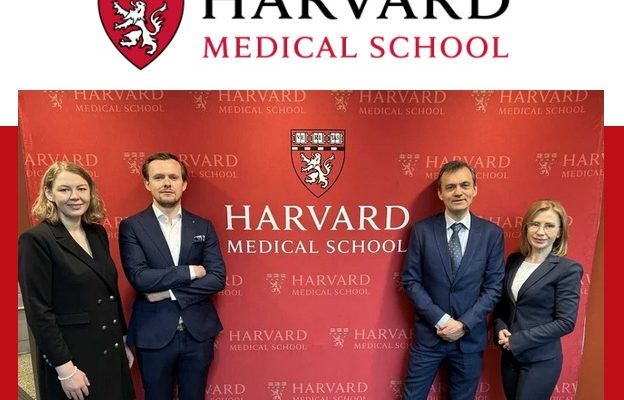 Laureaci studiów pozują na tle ścianki z logo Harvardu.