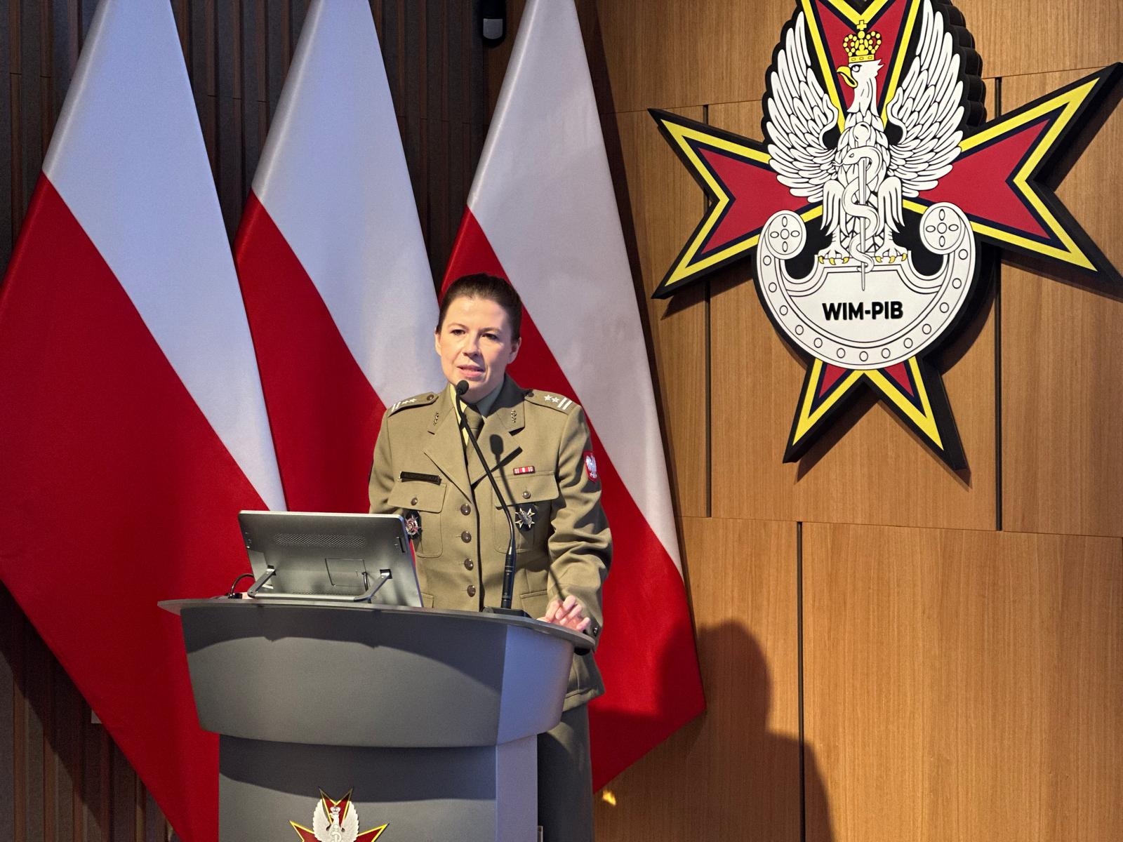 Panelistka przy mównicy, za nią logo WIM i flagi Polski.