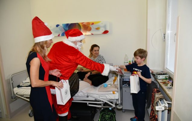 Święty Mikołaj i Małgorzata Złotkowska w czapce świętego Mikołaja wręczają prezent chłopcu.