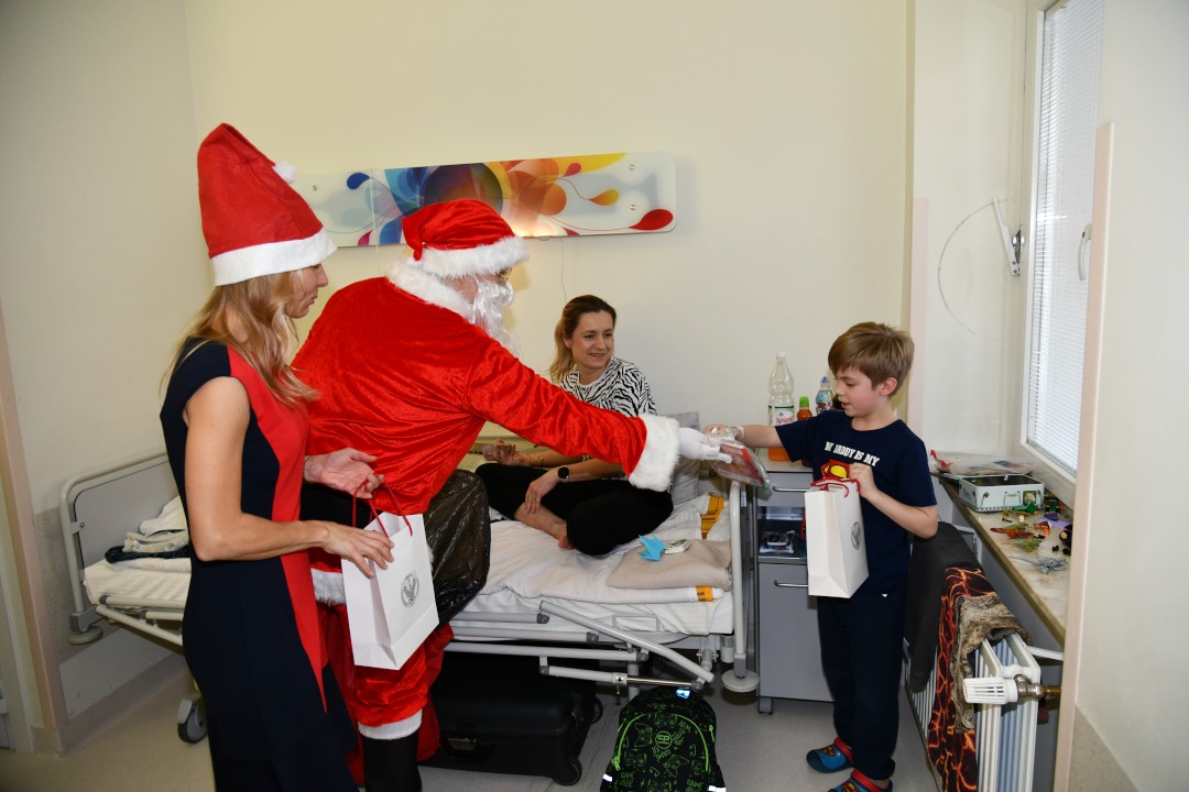 Święty Mikołaj i Małgorzata Złotkowska w czapce świętego Mikołaja wręczają prezent chłopcu.