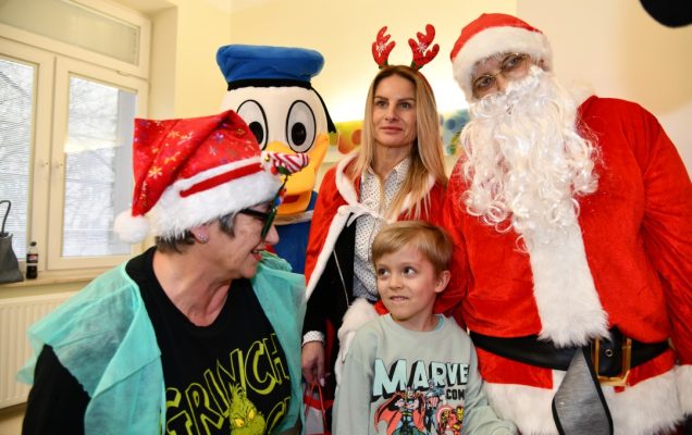 Mały pacjent z Mikołajem i jego pomocnikami pozują do zdjęcia na sali szpitalnej.