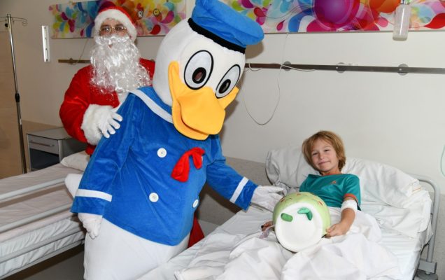 Sala szpitalna. Kaczor Donald przy łóżku wręcza prezent młodemu pacjentowi.