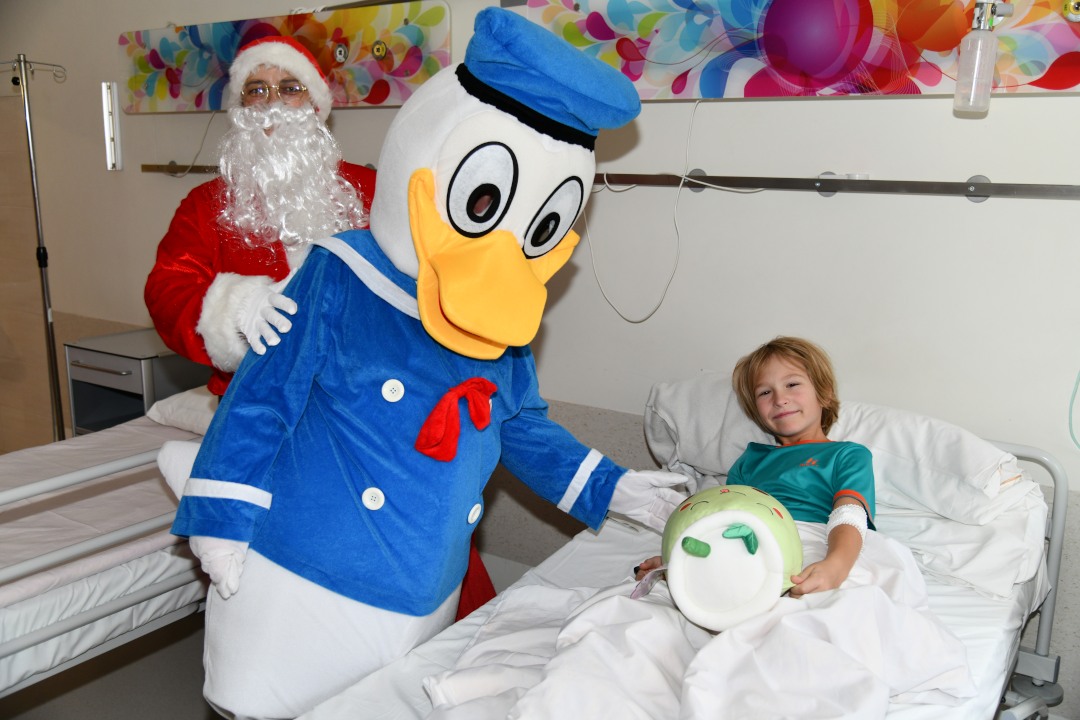 Sala szpitalna. Kaczor Donald przy łóżku wręcza prezent młodemu pacjentowi.