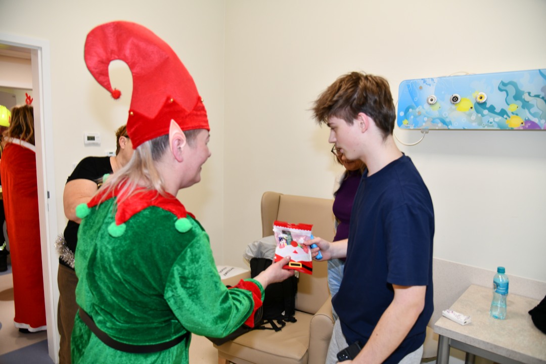 Sala szpitalna. Pani elfowa wręcza prezent nastoletniemu pacjentowi.