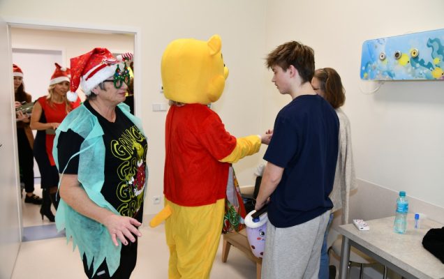 Sala szpitalna. Kubuś Puchatek wręcza prezent nastoletniemu pacjentowi.