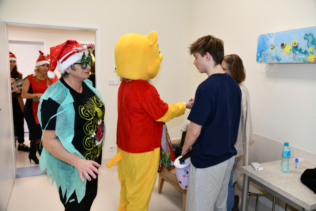 Sala szpitalna. Kubuś Puchatek wręcza prezent nastoletniemu pacjentowi.