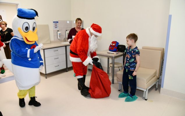 Święty Mikołaj w towarzystwie Kaczora Donalda daje prezent kilkuletniemu pacjentowi.