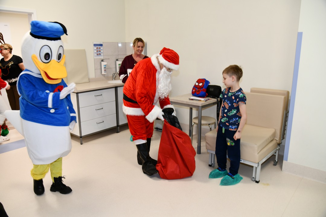 Święty Mikołaj w towarzystwie Kaczora Donalda daje prezent kilkuletniemu pacjentowi.