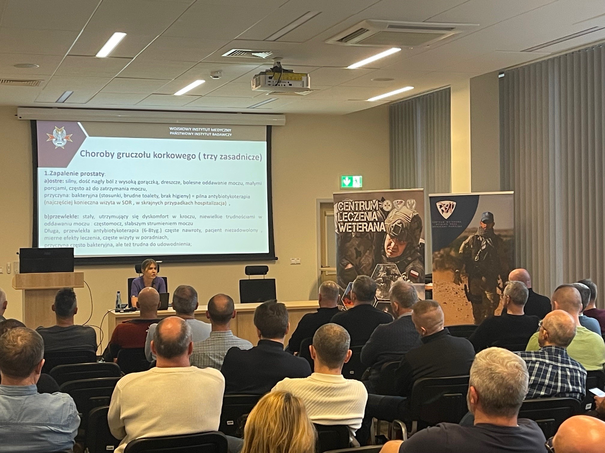 Ujęcie z tyłu. Siedzący uczestnicy na sali słuchający wykładu.