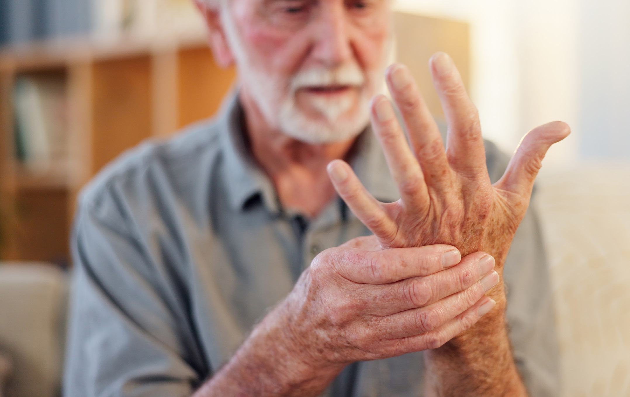 Starszy mężczyzna przytrzymuje dłonią drugą wyciągnietą przed siebie rękę.