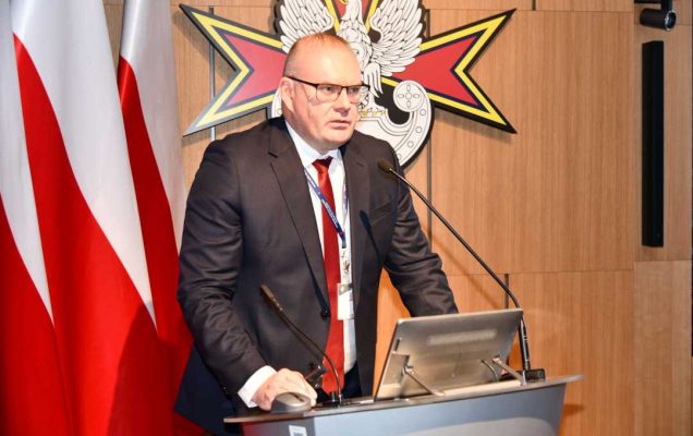 Bartosz Kulczakiewicz podczas przemówienia. Za nim logo Wojskowego Instytutu Medycznego.