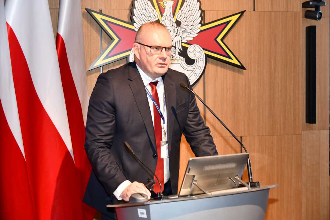 Bartosz Kulczakiewicz podczas przemówienia. Za nim logo Wojskowego Instytutu Medycznego.