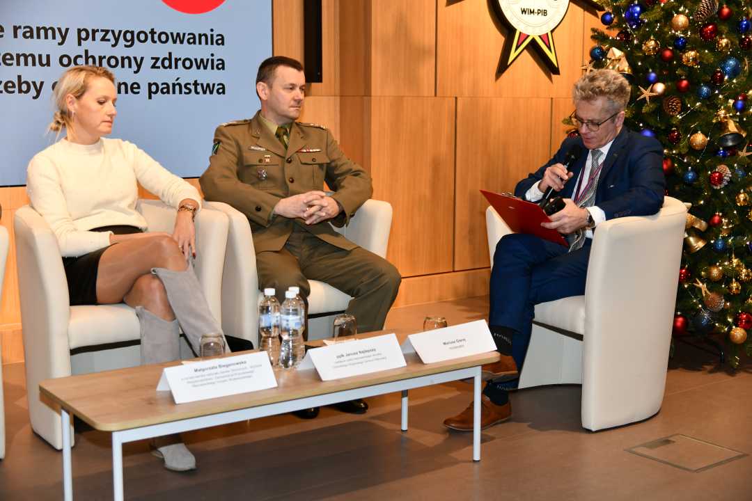 Siedzący w fotelach paneliści podczas sesji, za nimi fragment wyświetlanej prezentacji.