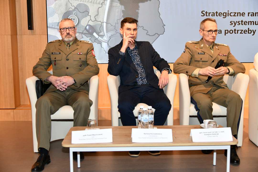 Generał broni Grzegorz Gielerak siedzący z panelistami podczas sesji, za nimi fragment wyświetlanej prezentacji.