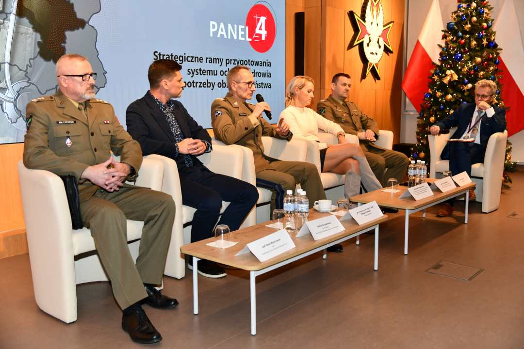 Dyrektor WIM Grzegorz Gielerak z panelistami podczas sesji, zabiera głos. Za nimi fragment wyświetlanej prezentacji.