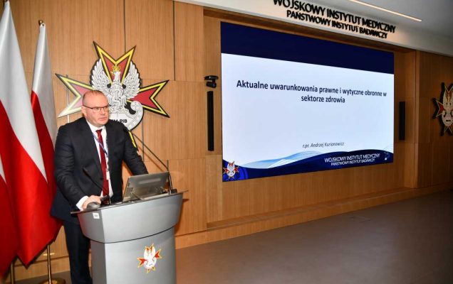 Bartosz Kulczakiewicz podczas przemówienia. Za nim na ekranie slajd tytułowy z konferencji.