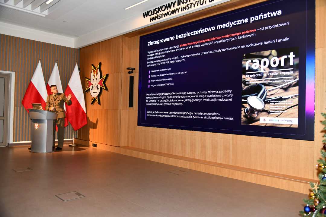 Jarosław Kowal przy mównicy podczas wykładu . Za nim na ekranie plansza tytułowa panelu.