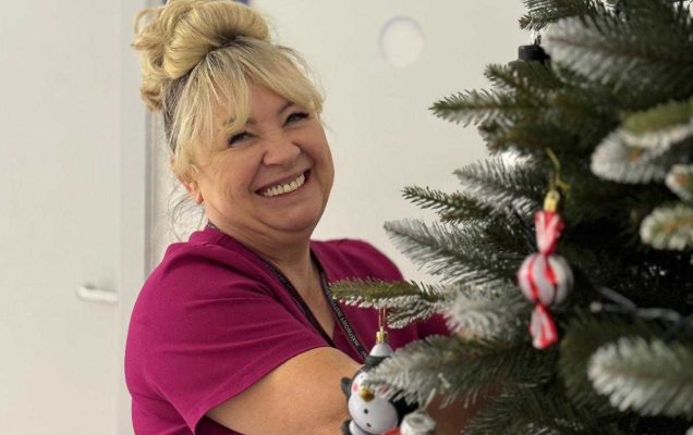 Uśmiechnięta pracowniczka wiesza ozdoby na choince.