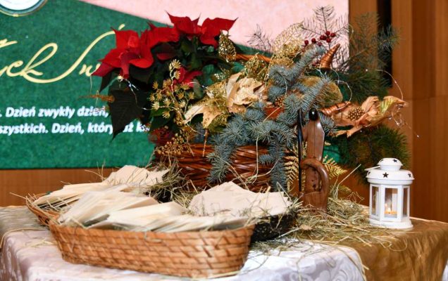 Koszyczek z siankiem i opłatkiem, obok stroik bożonarodzeniowy.