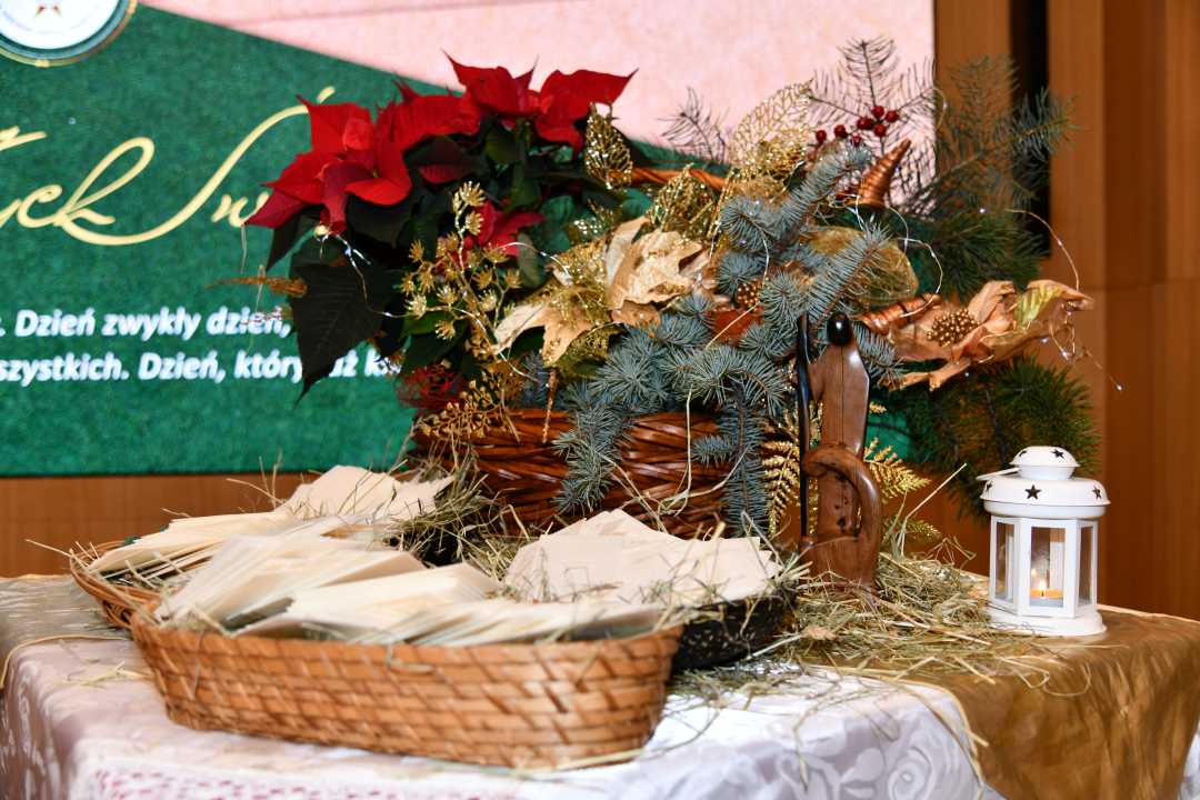 Koszyczek z siankiem i opłatkiem, obok stroik bożonarodzeniowy.
