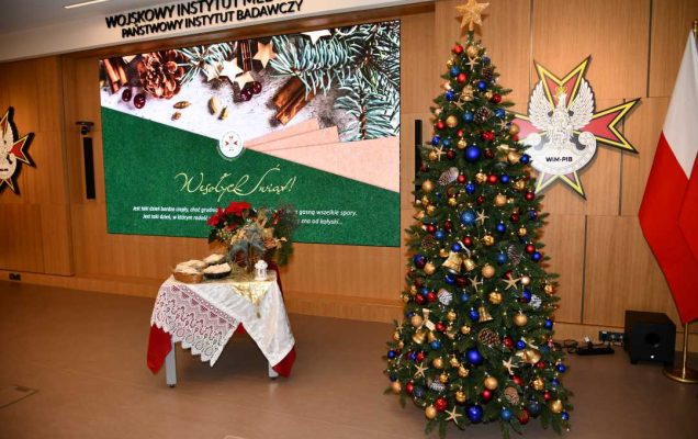 Aula WIM udekorowana świątecznie. Z prawej strony stoi olbrzymia choinka, obok stolik z opłatkiem, na ekranie wyświetlona plansza świąteczna z życzeniami.