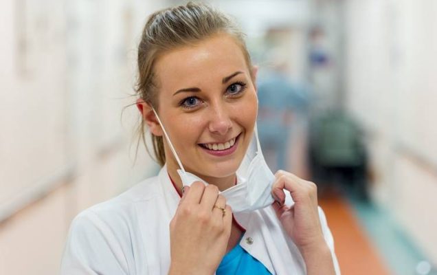 pielęgniarka na korytarzu szpitalnym, uśmiechnięta z zsuniętą z twarzy maseczką