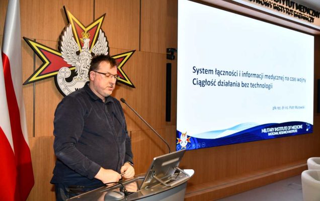 Piotr Murawski przy mównicy za jego plecami na ekranie slajd z konferencji.