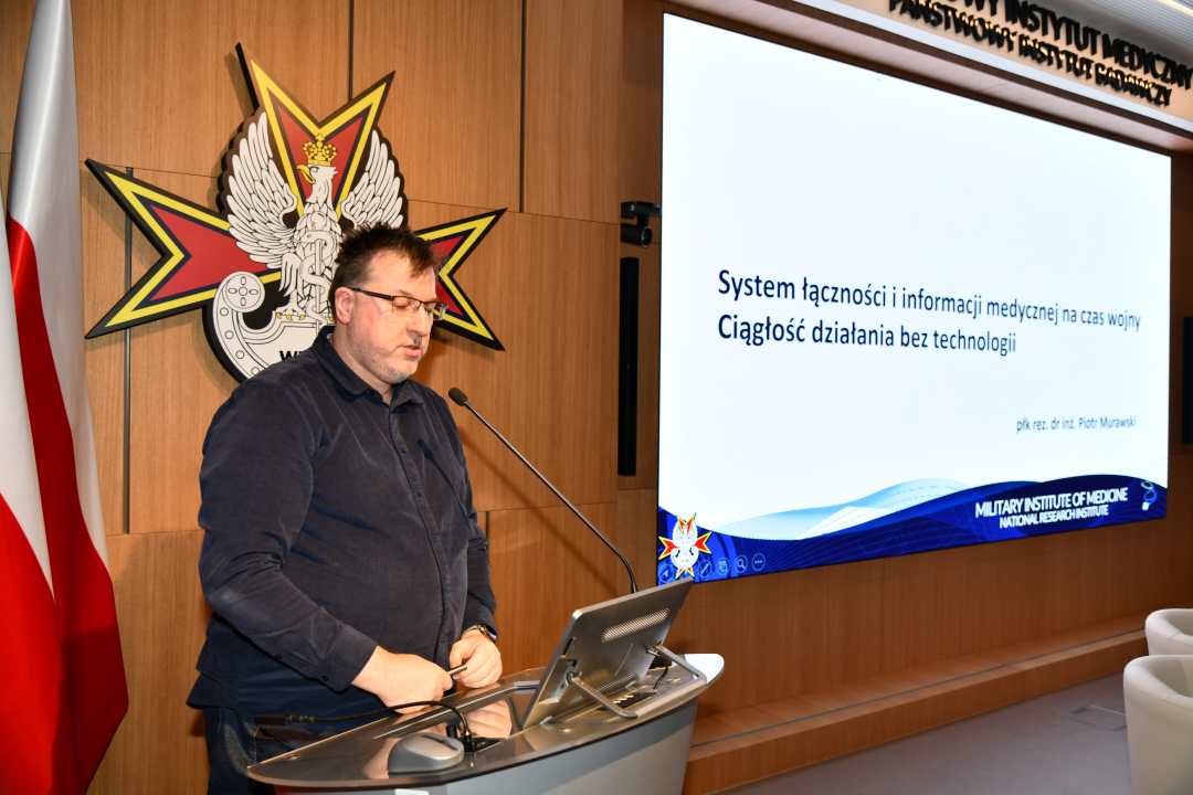 Piotr Murawski przy mównicy za jego plecami na ekranie slajd z konferencji.