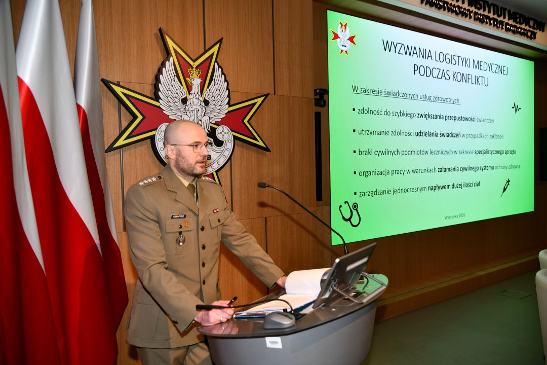 mgr Bartłomiej Kwapisz przy mównicy, za nim na ekranie wyświetlona prezentacja.