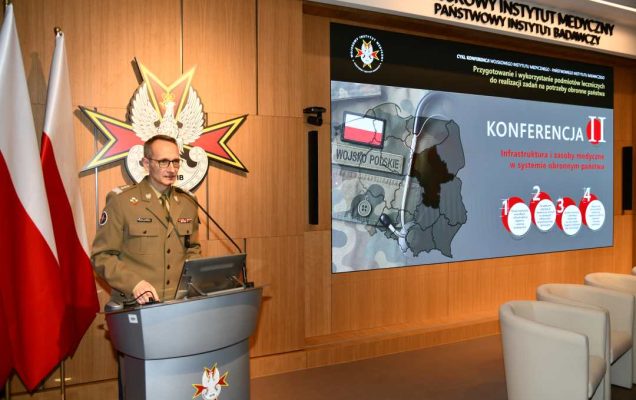 Grzegorz Gielerak przy mównicy, za jego plecami na ekranie prezentacja konferencyjna.