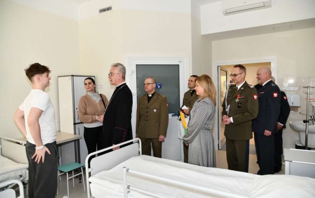 Biskup, dyrektor WIM oraz pracownicy szpitala z wizytą na sali chorych w Klinice pediatrii. Biskup rozmawia na sali z nastolatkiem.