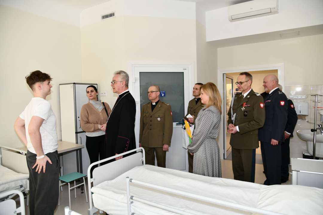 Biskup, dyrektor WIM oraz pracownicy szpitala z wizytą na sali chorych w Klinice pediatrii. Biskup rozmawia na sali z nastolatkiem.