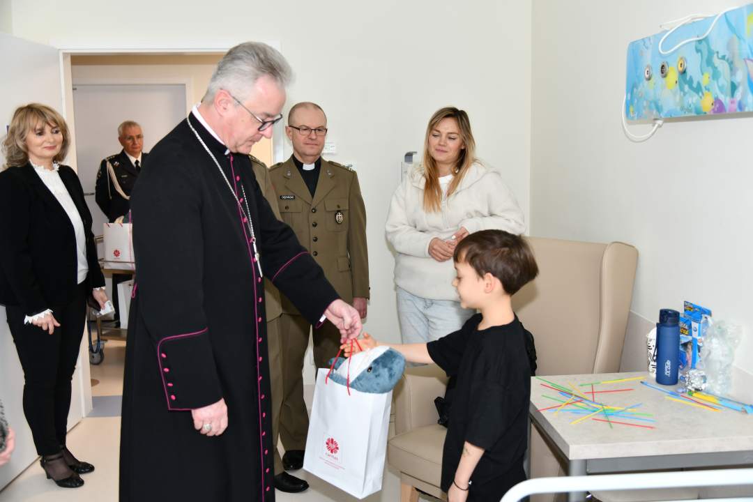 Biskup, dyrektor WIM oraz pracownicy szpitala z wizytą na sali chorych w Klinice pediatrii. Biskup wręcza torbę z prezentem chłopcu.