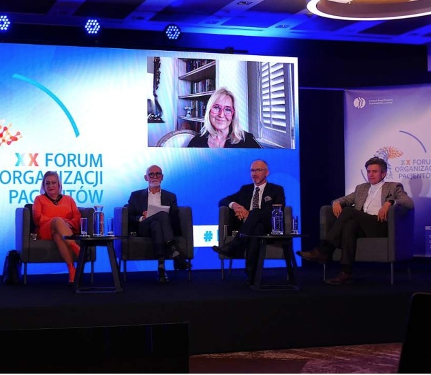 Uczestnicy forum siedzący w fotelach podczas dyskusji panelowej. Za nimi ekran z transmisją spotkania.